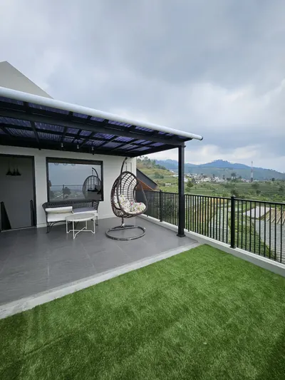 Rooftop dengan rumput artifisial dengan kursi ayun rotan dan pagar, menghadap ladang dan perbukitan kaki Gunung Slamet